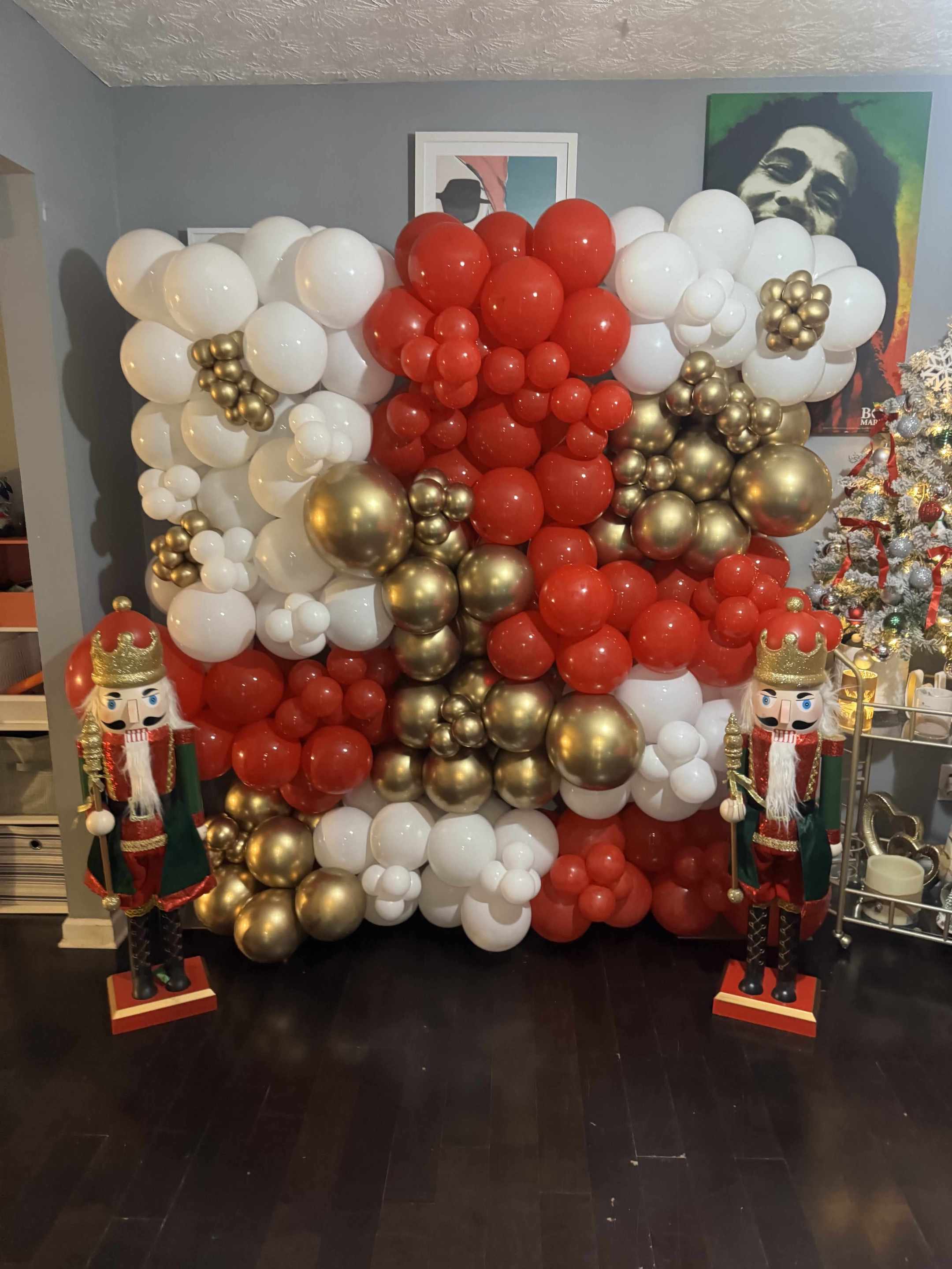 Balloon arch with red, white, and gold balloons in a room with nutcrackers and a Christmas tree.