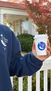 Person holding a white coffee cup with a logo outdoors