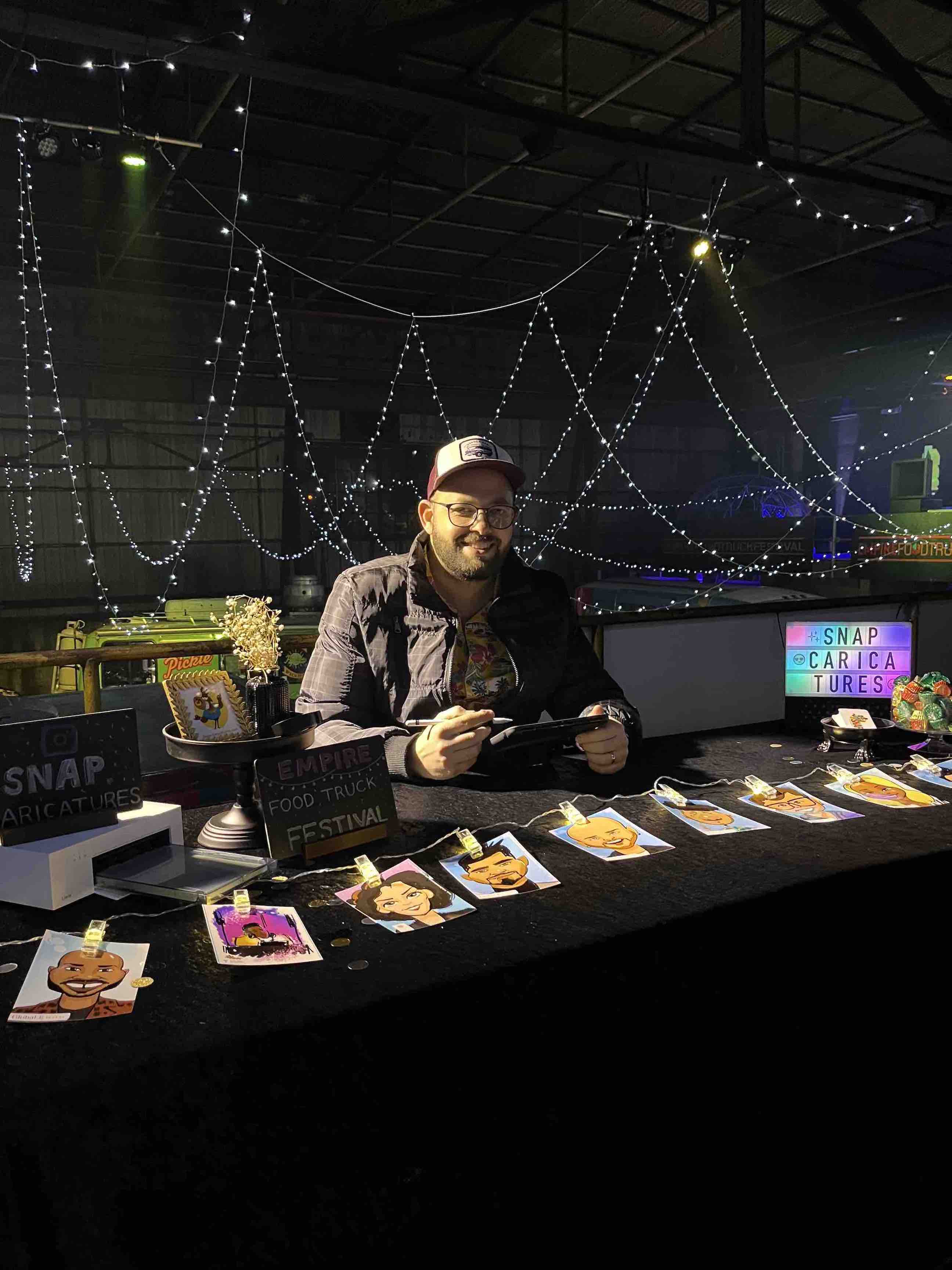 Man sitting at a table drawing digital caricatures in Atlanta surrounded by string lights and a cityscape view.
