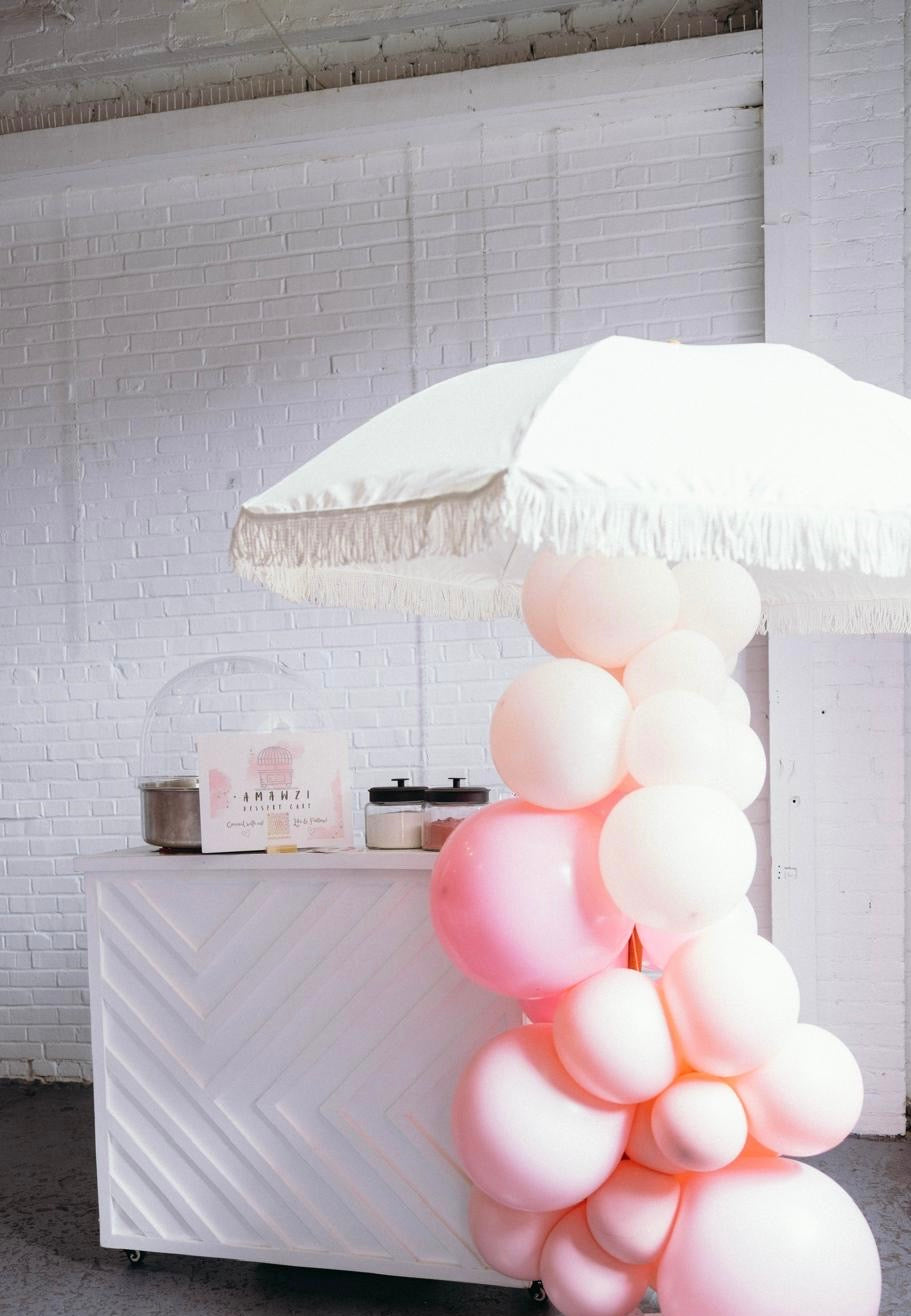 Decorative balloon arch with pink and white balloons on a white table against a white brick wall.