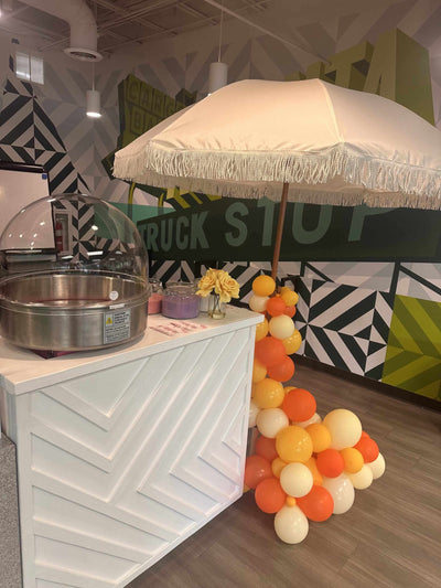 Decorative dessert cart for events in Atlanta with a white umbrella, balloons, and a geometric-patterned wall.
