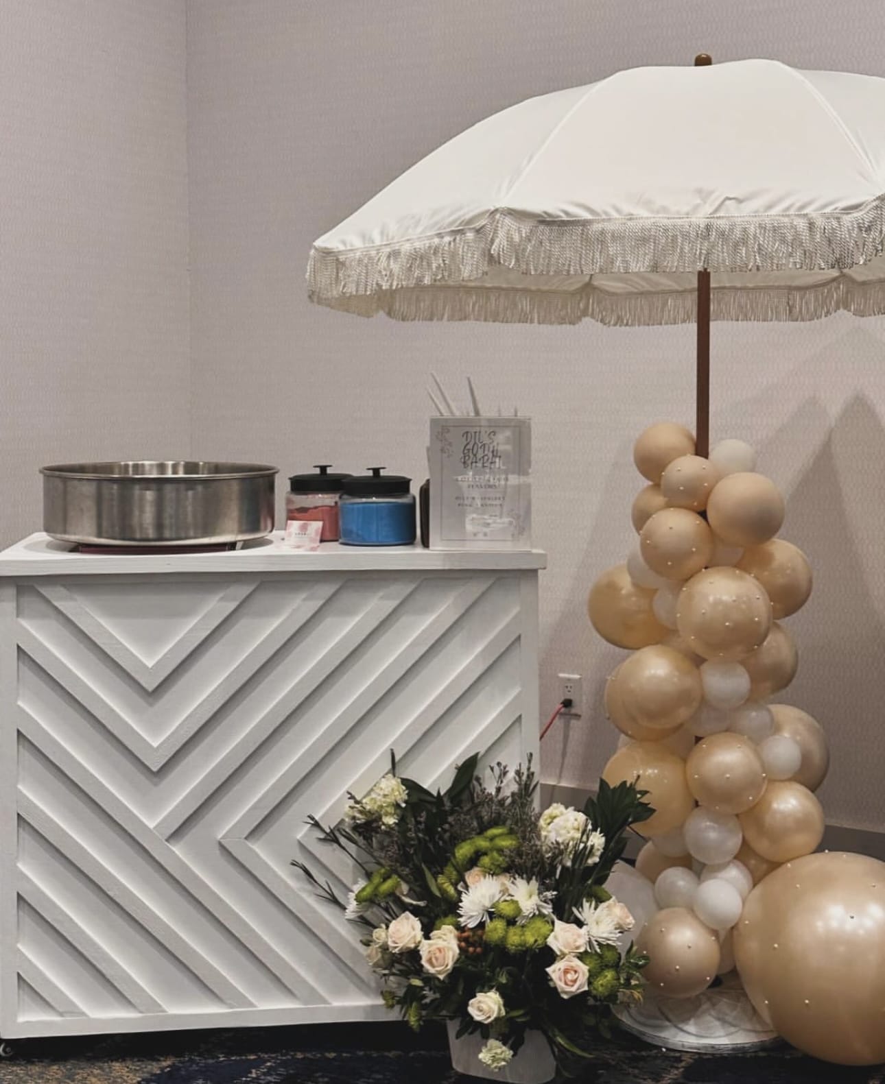 Decorative dessert cart in Atlanta with a white umbrella, geometric-patterned cabinet, balloons, and flowers.