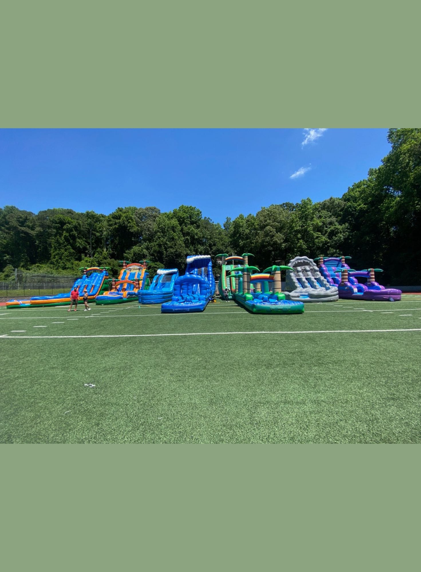 Colorful inflatable water slides on a grassy field with trees in the background