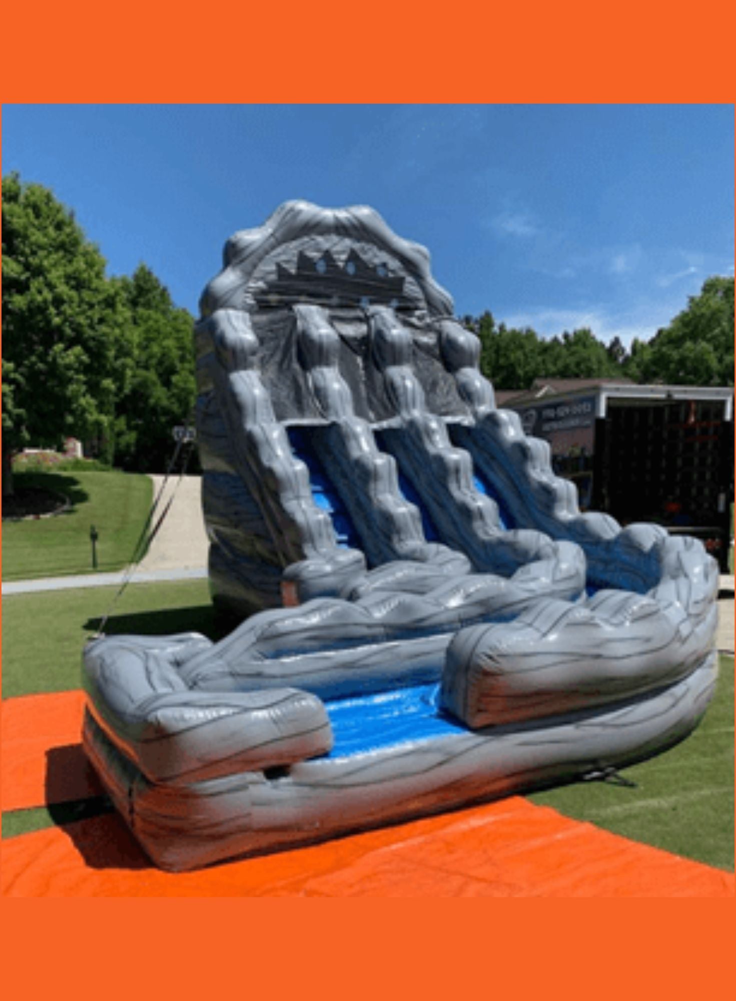 Inflatable water slide on a grassy field with trees and a clear sky in the background.