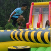 Child jumping on an inflatable slide with a colorful inflatable obstacle course in the background.