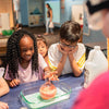 Children engaged in a science experiment at a table with a teacher observing.