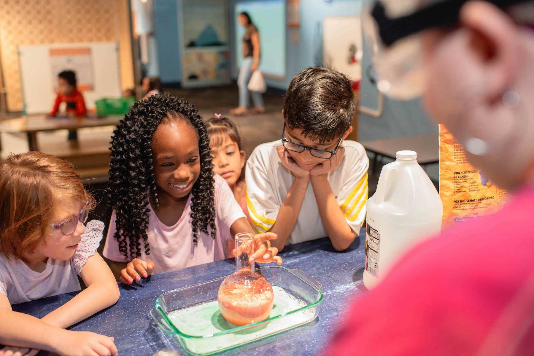 Children engaged in a science experiment at a table with a teacher observing.