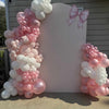 Balloon arch with pink and white balloons in front of a white board with a pink bow design.