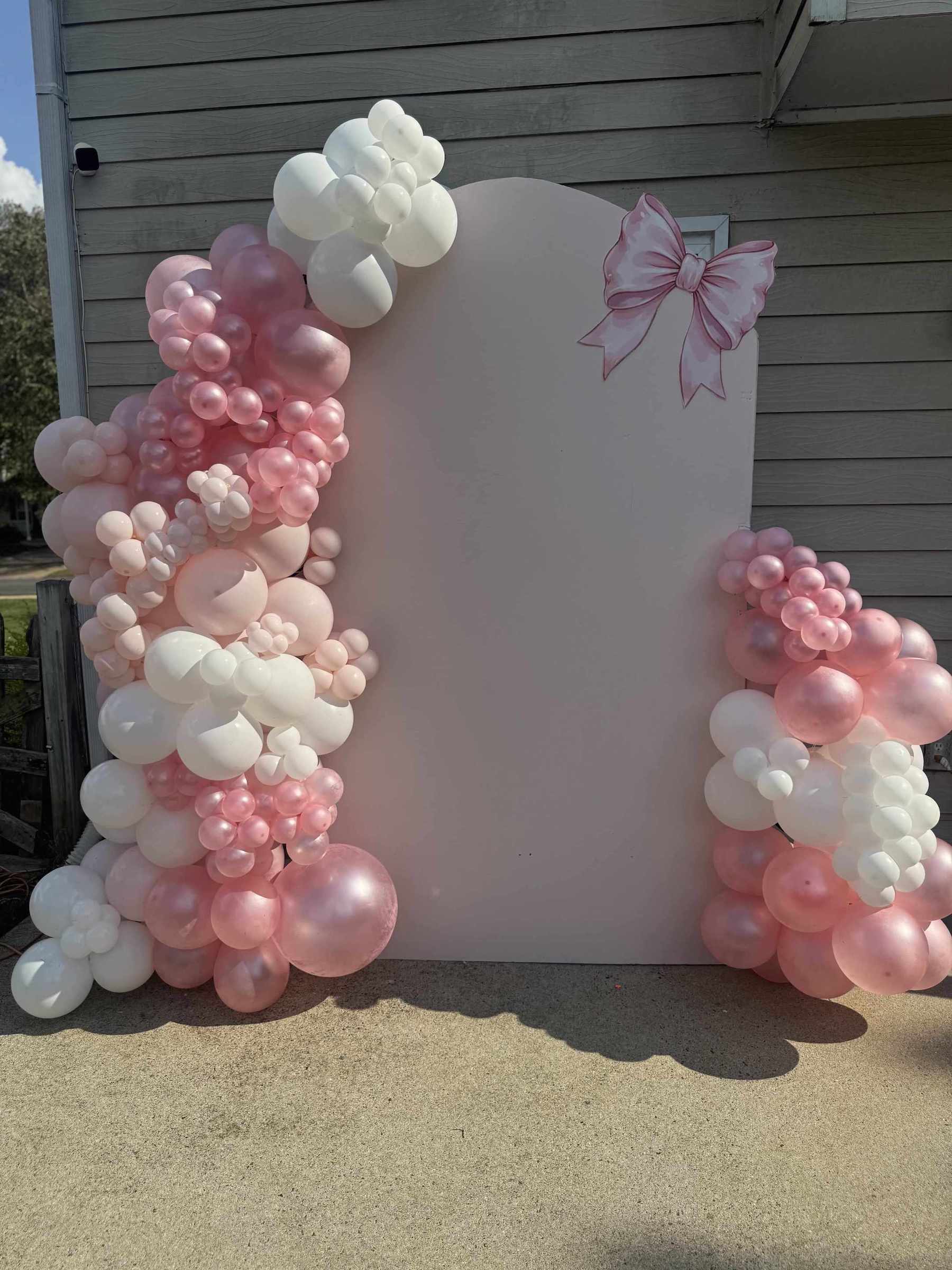 Balloon arch with pink and white balloons in front of a white board with a pink bow design.