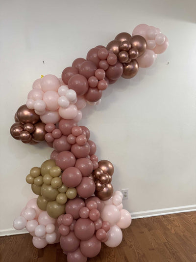Balloon arch with pink, gold, and rose gold balloons against a white wall.