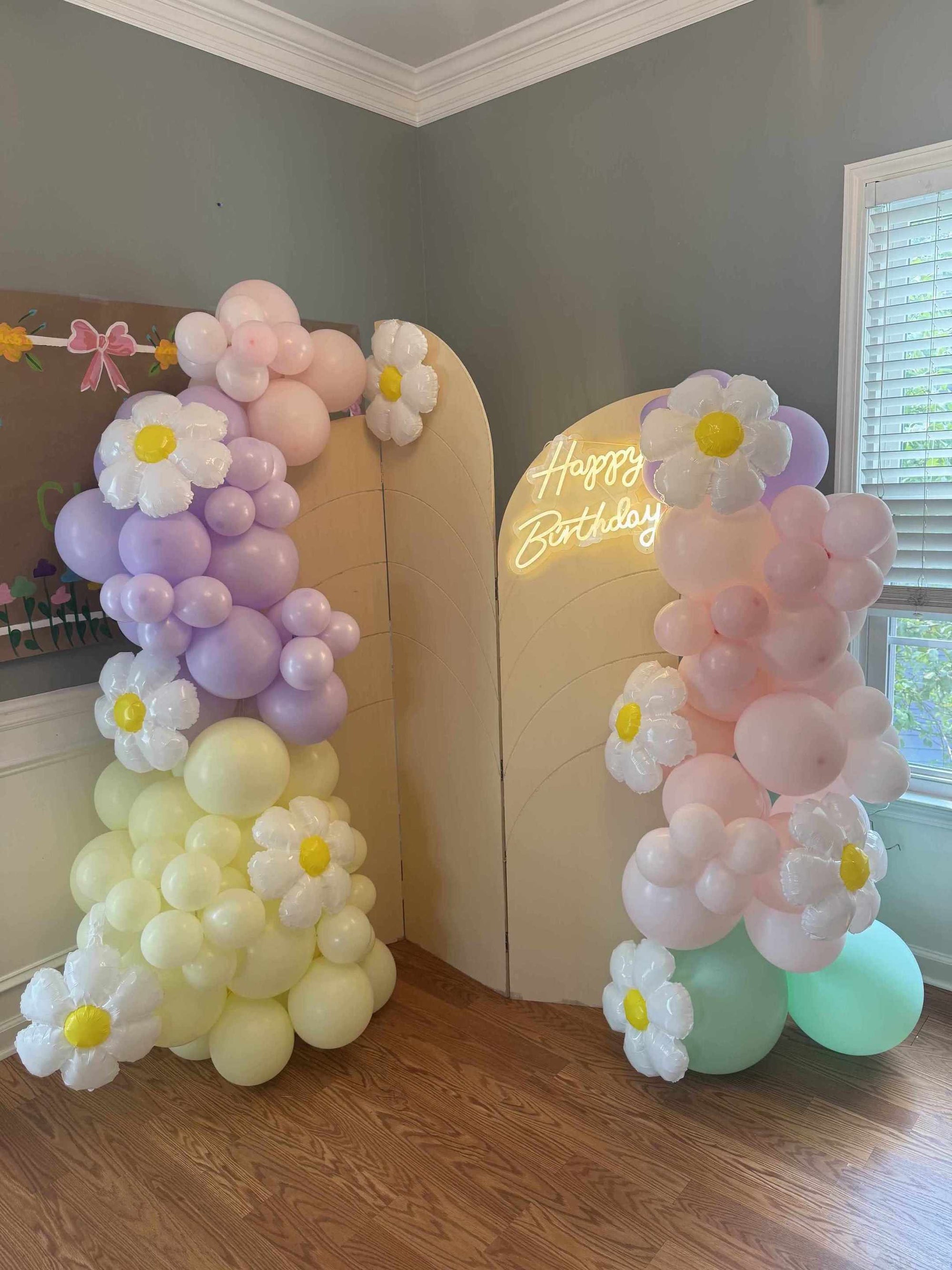 Pastel-colored balloon arch with flower decorations in a room.