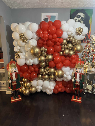 Balloon arch with red, white, and gold balloons in a room with nutcrackers and a Christmas tree.