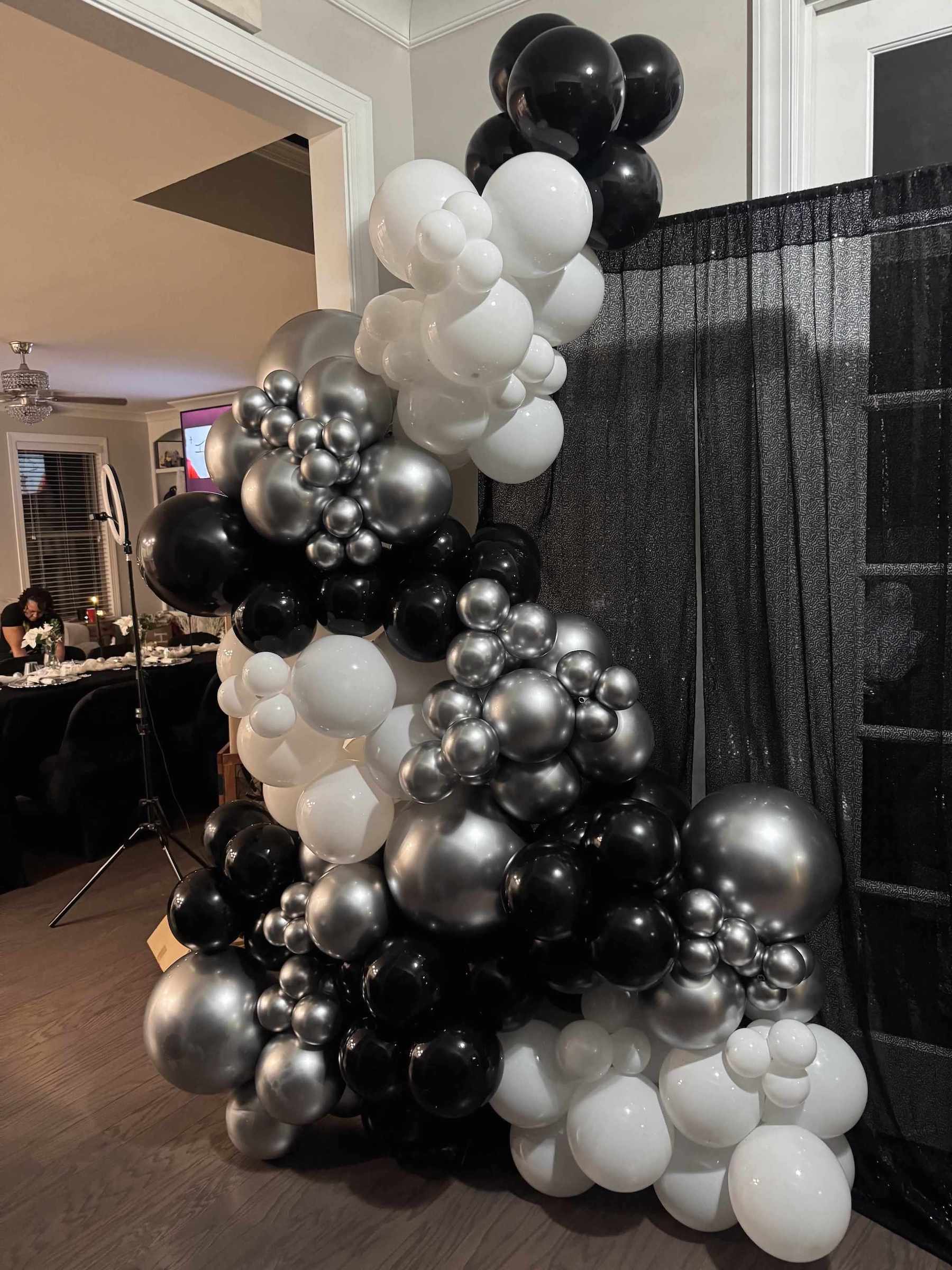 Balloon arch with black, white, and silver balloons in a room setting.