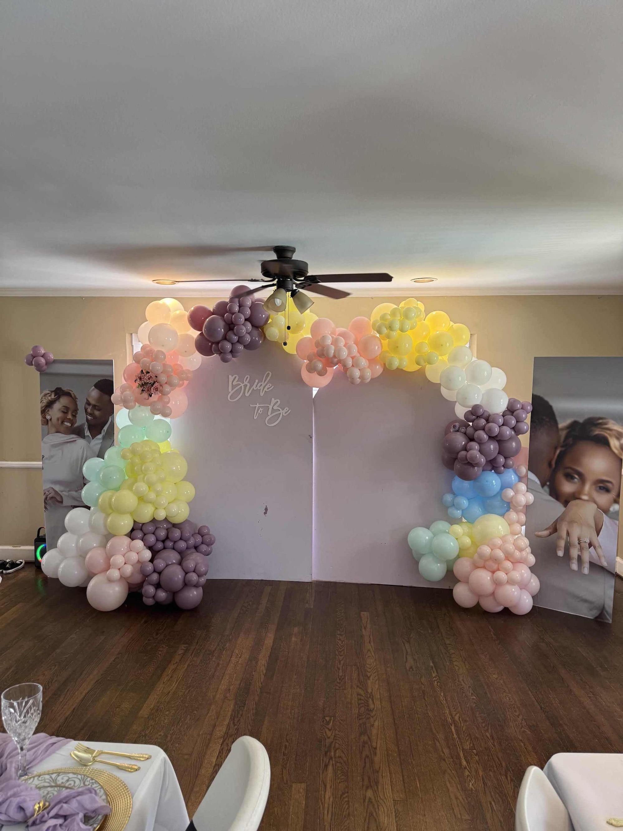 Balloon arch with pastel colors in a room with tables and chairs.