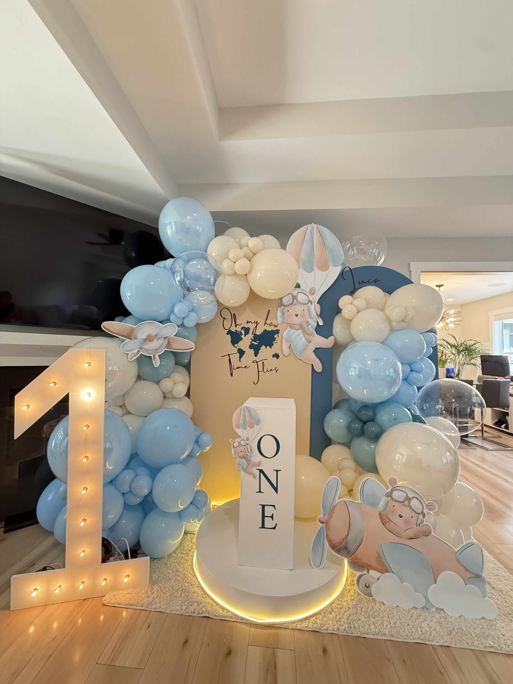 Balloon arch with baby-themed decorations and a 'ONE' sign in a room.