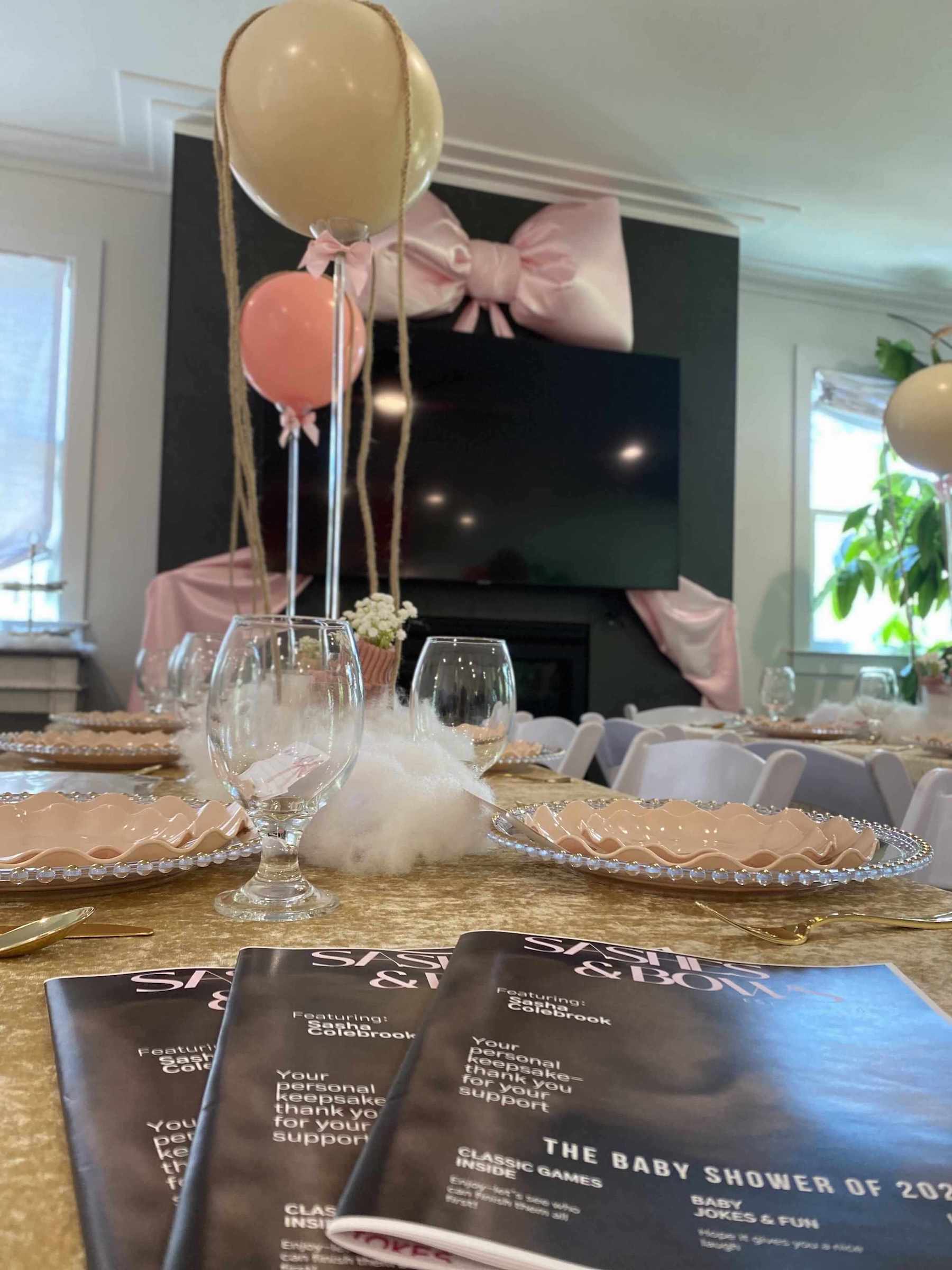 Decorated table with balloons and baby shower programs in a room with a TV in the background for a baby shower in Atlanta.