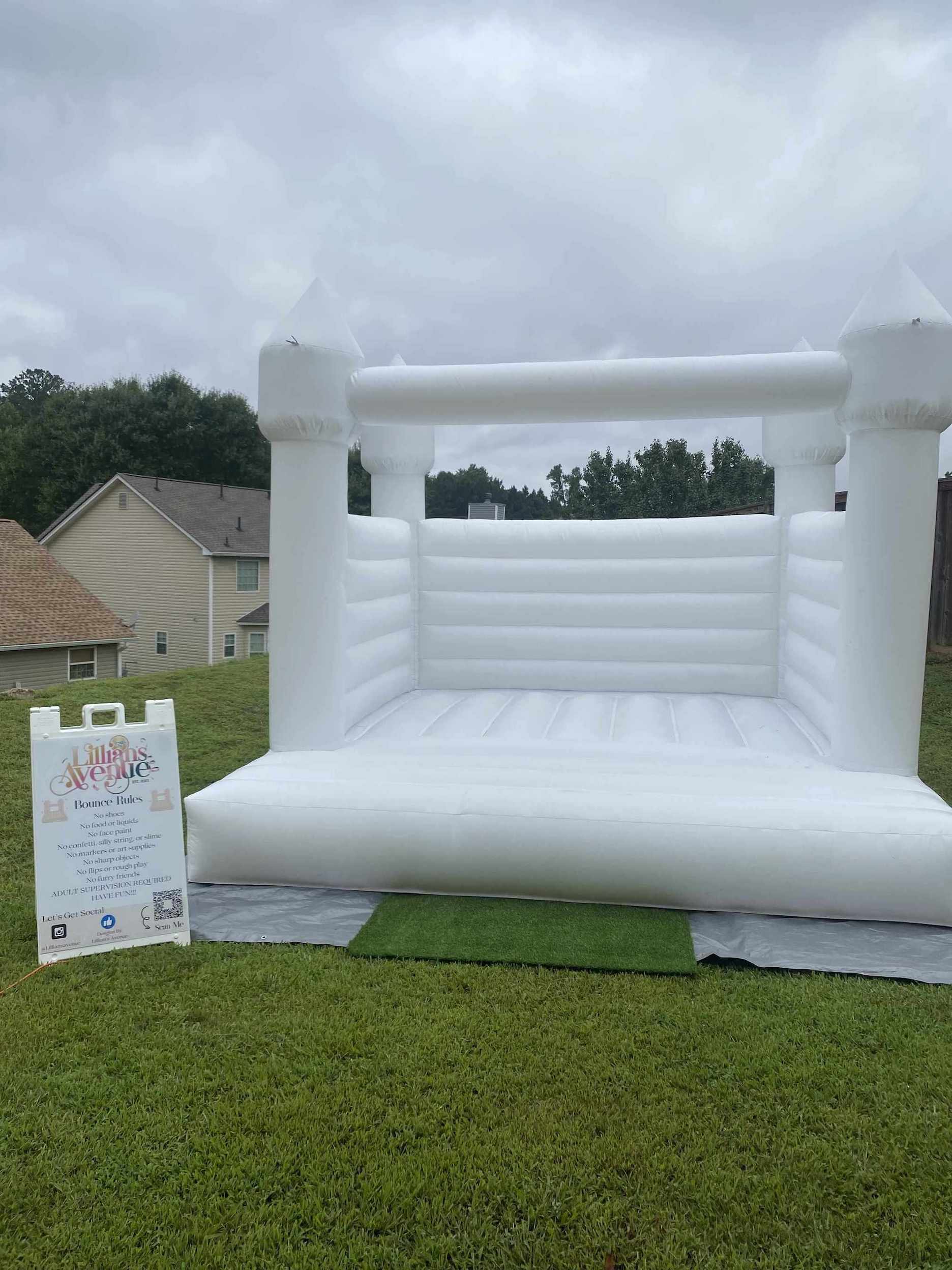Inflatable white bounce house on grass with a sign in the foreground