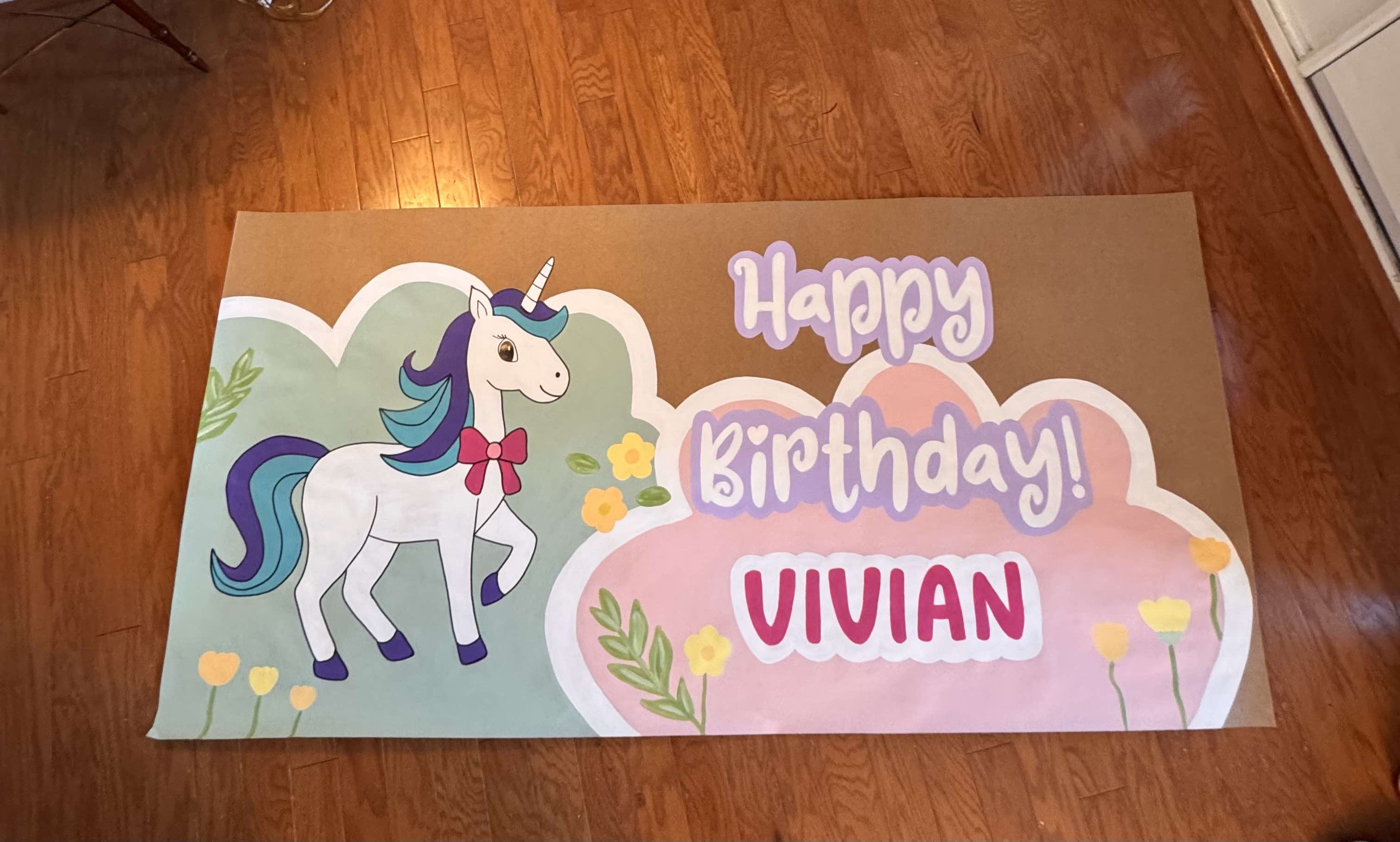Custom hand-painted banner with a unicorn illustration and 'Happy Birthday Vivian' text on a wooden floor.