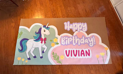 Custom hand-painted banner with a unicorn illustration and 'Happy Birthday Vivian' text on a wooden floor.
