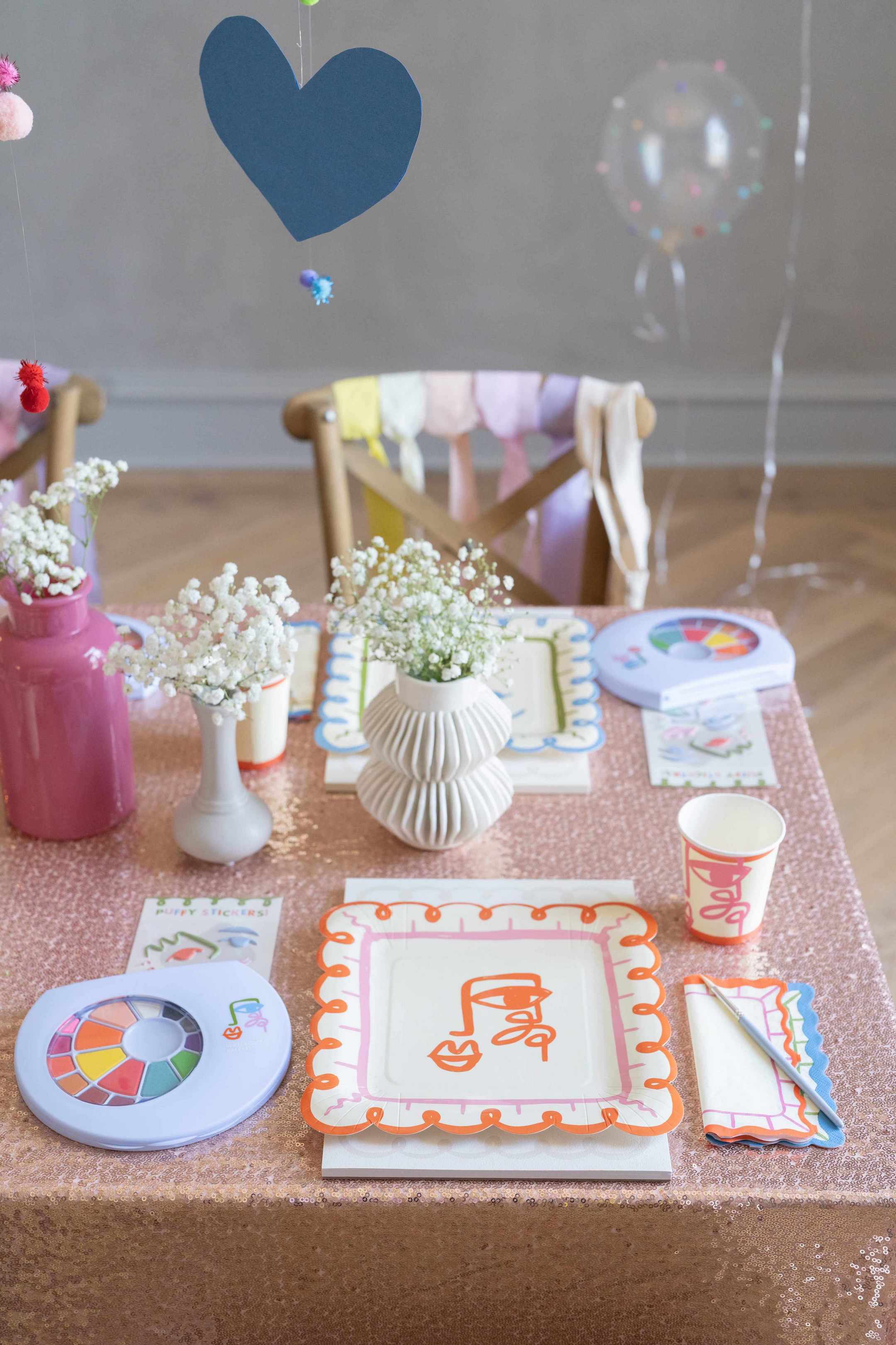 Kids birthday party supplies on a party table setup with plates, cups, and decorations on a wooden floor.