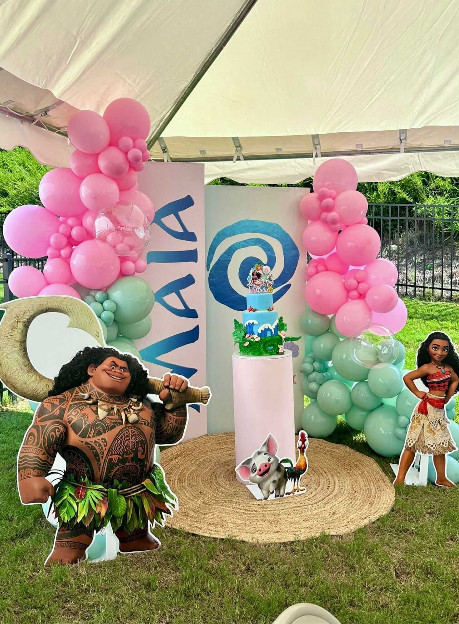 Decorative setup with Moana-themed elements including balloons, a cake, and character cutouts under a tent.