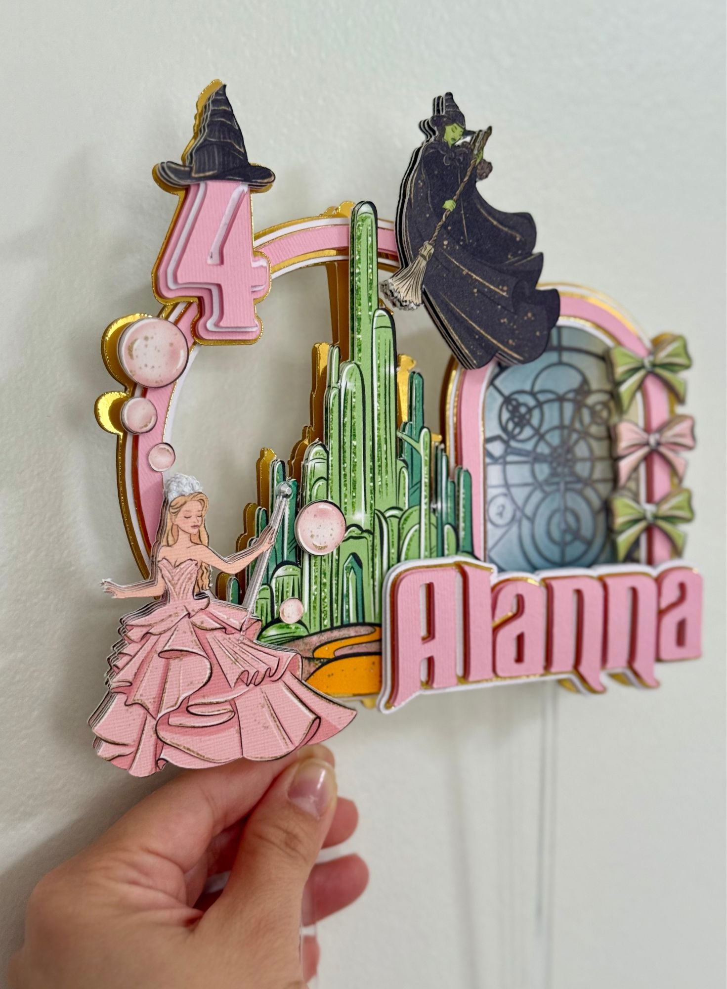 Decorative birthday number with princess and witch design, held by a hand.