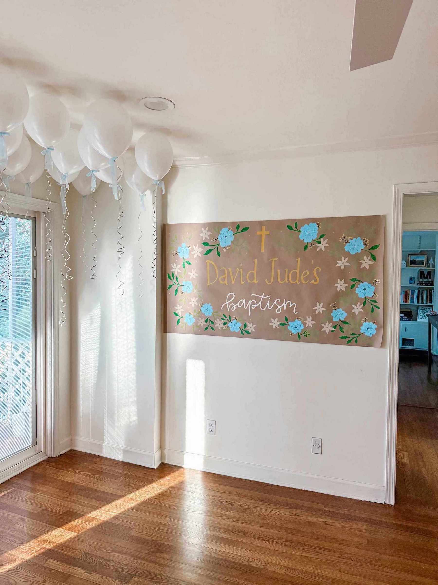 Painted banner with floral designs and text on a wall in a room with wooden flooring and balloons.