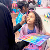 Child getting makeup applied with a colorful palette in a spa party bus.