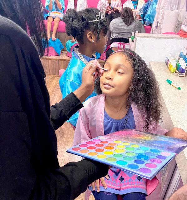 Child getting makeup applied with a colorful palette in a spa party bus.