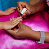 Girls getting her nails painted with purple nail polish on a pink surface.
