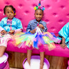 Children in colorful outfits sitting on a pink bench getting pedicures at a spa bus party in Atlanta.