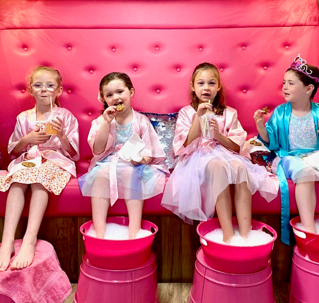 Four girls in colorful dresses sitting on a pink couch with pink buckets filled with bubbles for a girls birthday party in Atlanta.
