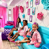 Three children in pink robes sitting on a blue couch in a playroom with decorative walls and furniture.