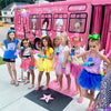 Group of children in front of a pink party bus with cartoon characters on the side.