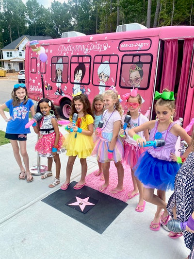 Group of children in front of a pink party bus with cartoon characters on the side.