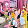 Group of children in colorful costumes in front of a pink party bus for a birthday party.