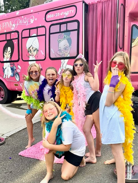 Group of children in colorful costumes in front of a pink party bus for a birthday party.