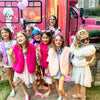 Group of children in front of a pink party bus with cartoon characters on the side for a birthday party.