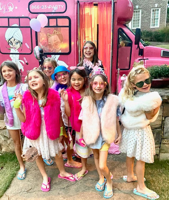 Group of children in front of a pink party bus with cartoon characters on the side for a birthday party.