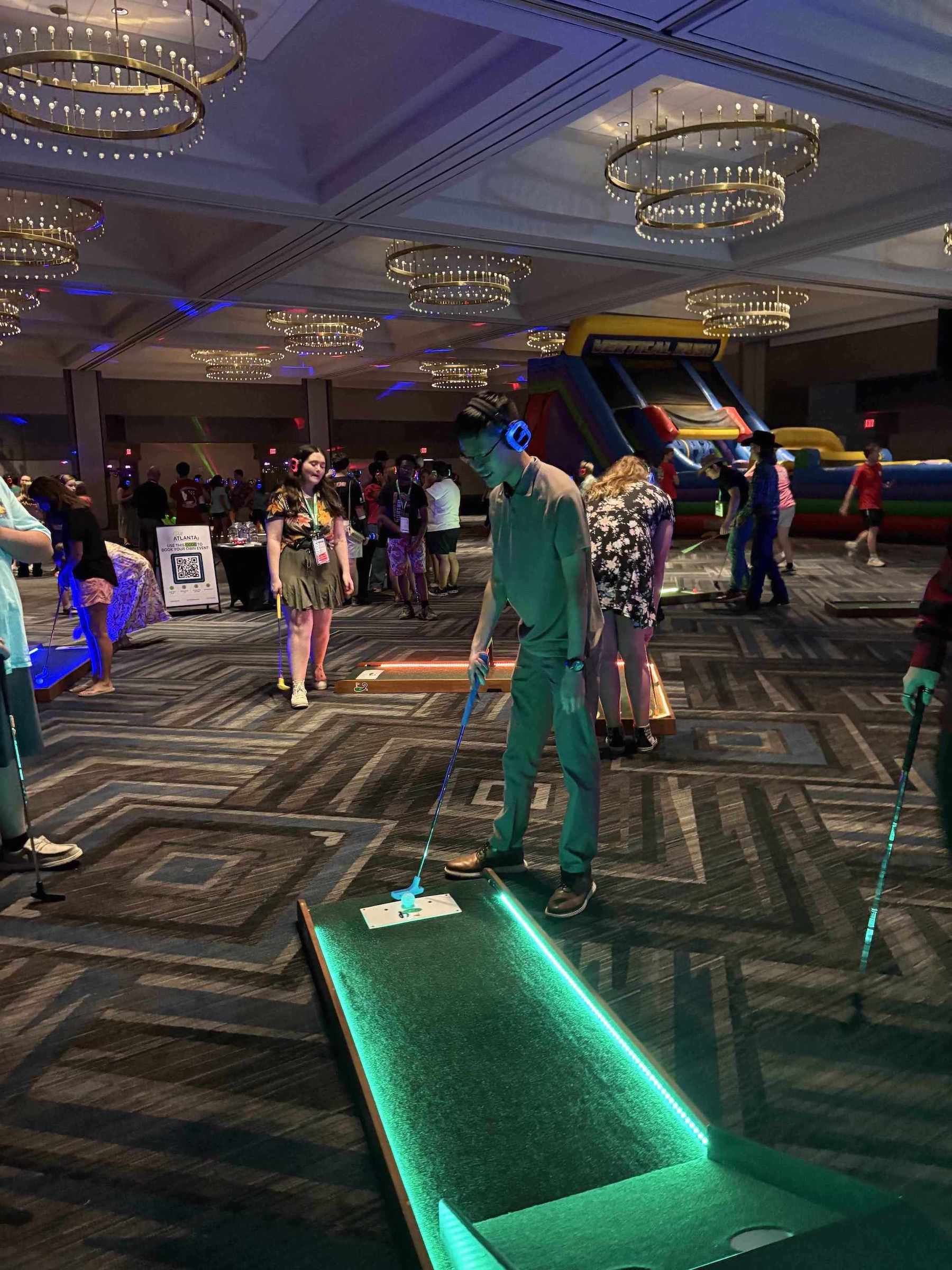 Teen playing a mini golf game in a large indoor venue with an inflatable slide at a teen birthday party in Atlanta GA | Confetti Jar