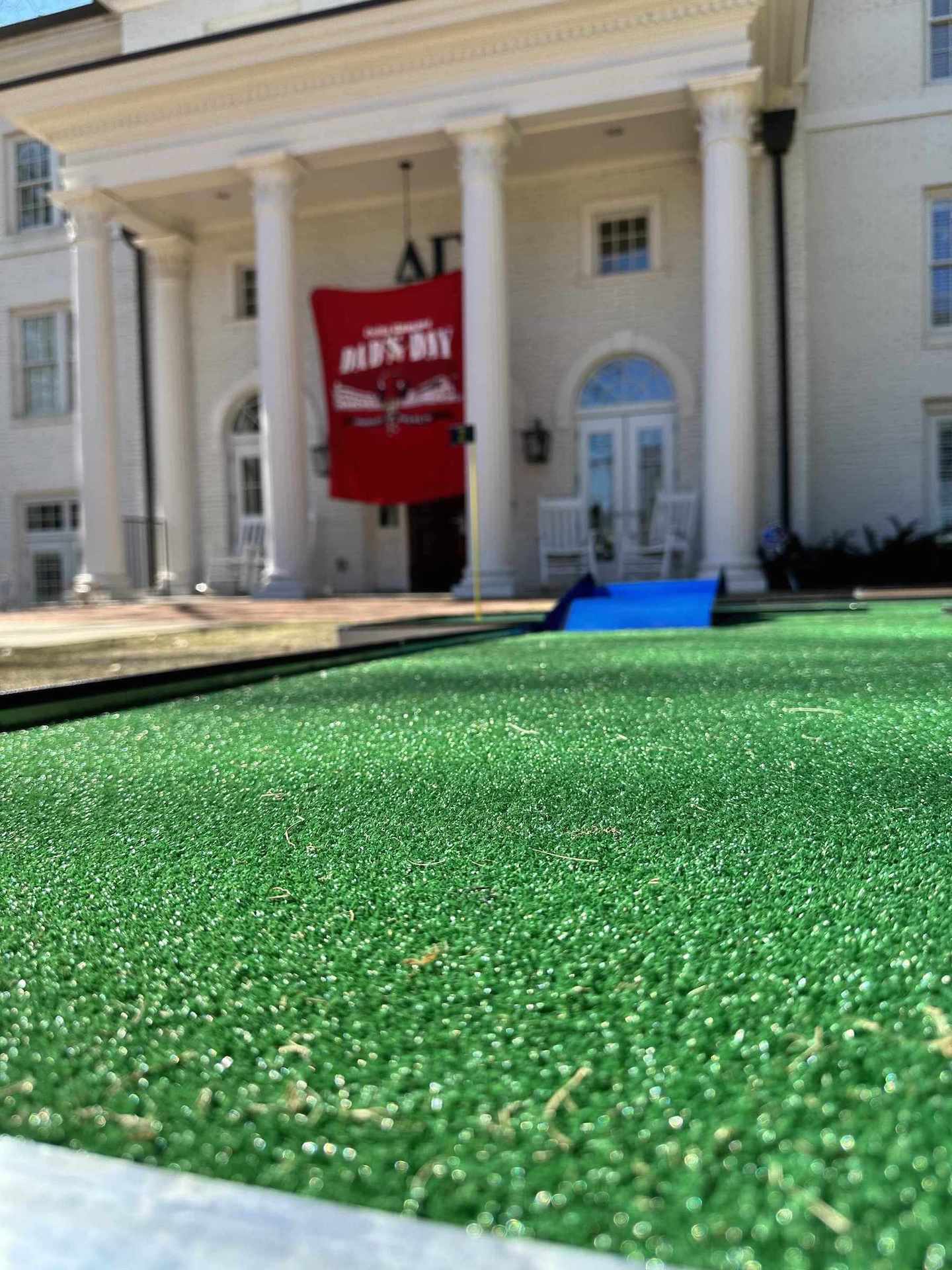 Green artificial grass for a mobile mini golf in front of a large white building with columns | Confetti Jar