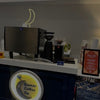Coffee shop counter with coffee-making equipment and a sign for Qamar Coffee Co.