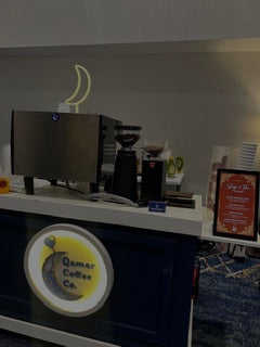 Coffee shop counter with coffee-making equipment and a sign for Qamar Coffee Co.