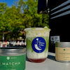 Matcha coffee and ingredients on a table with a blurred outdoor background