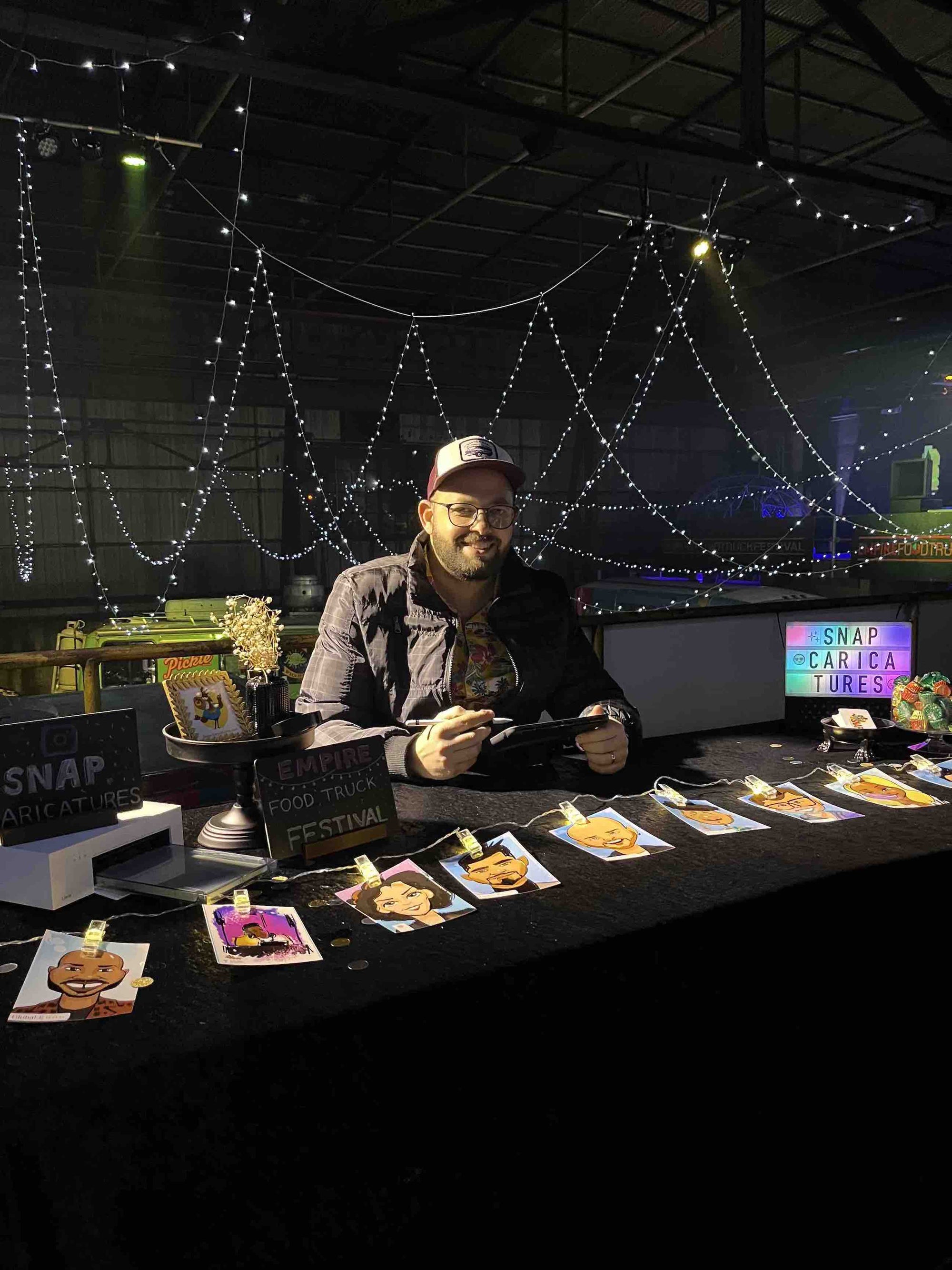 Man sitting at a table drawing digital caricatures  in Atlanta surrounded by string lights and a cityscape view.