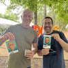Two men holding up cards with digital caricatures  in Atlanta of themselves outdoors under a tree.