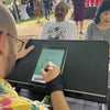 Person drawing digital caricatures  in Atlanta at an outdoor event with people in the background.