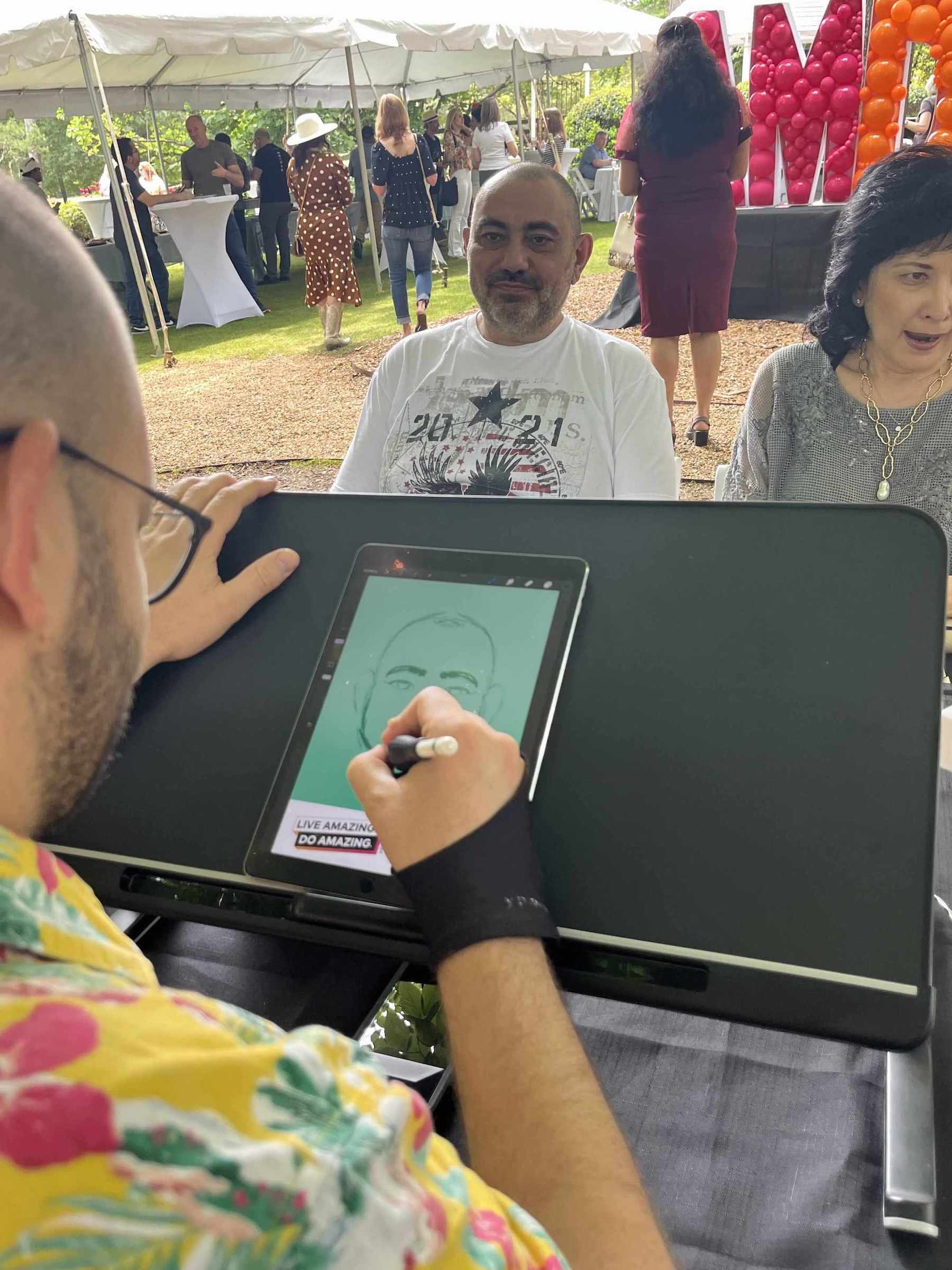 Person drawing digital caricatures  in Atlanta at an outdoor event with people in the background.