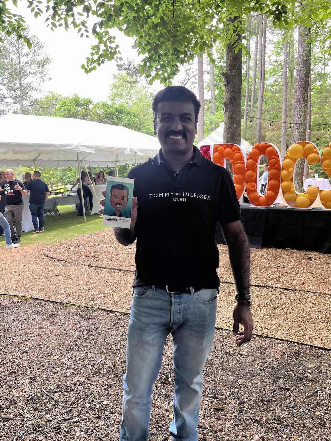 Man holding a digital caricature  in Atlanta at an outdoor event with trees and tents in the background.