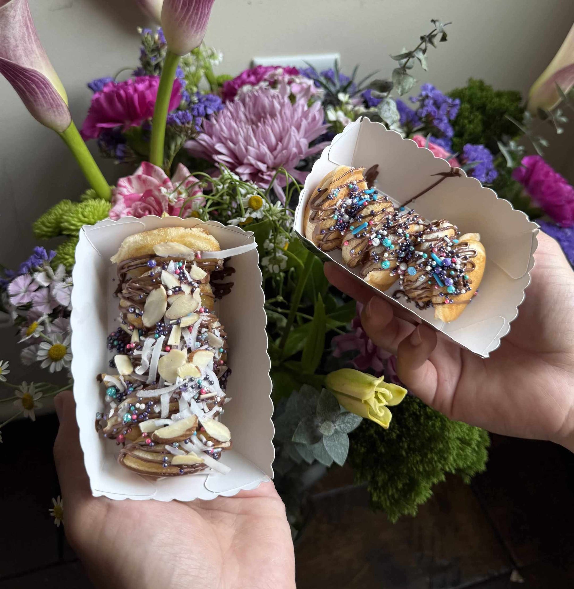 Two hands holding pastries with sprinkles in front of a floral arrangement | Pancake Cart Atlanta | Confetti Jar